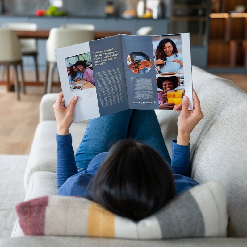 Woman laying down on a couch while looking through a magazine