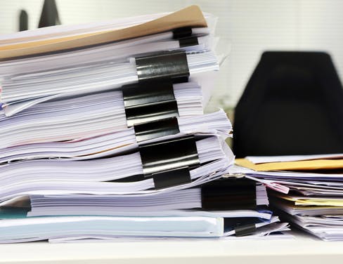 A huge stack of paper documents on a desk.