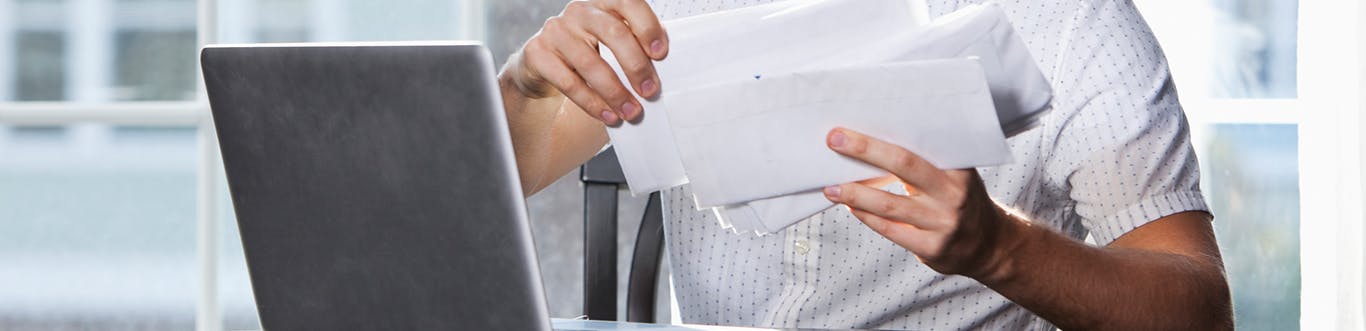 Man sorting through mail envelopes sitting at desk