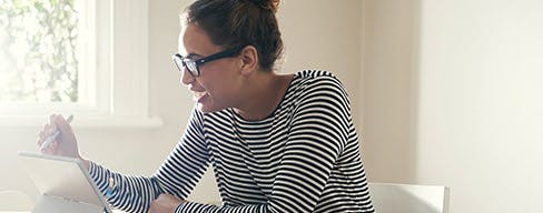 Photo of a girl in a striped shirt and glasses, smiling and working on a tablet.