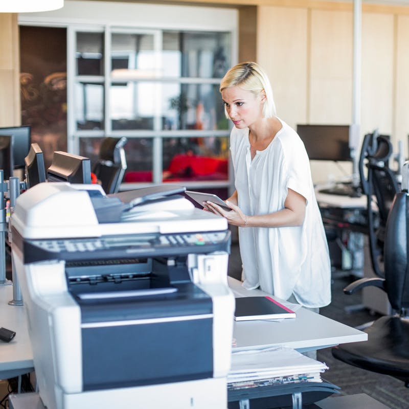 Female professional standing with digital tablet at office along side a printer.