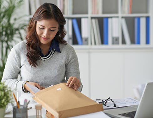 Ricoh - Lady in grey sweater preparing a package at her desk
