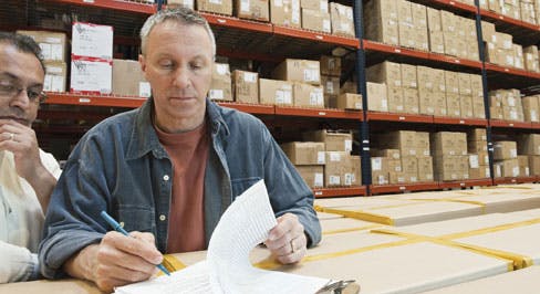 two men in a warehouse looking at paperwork on a clipboard