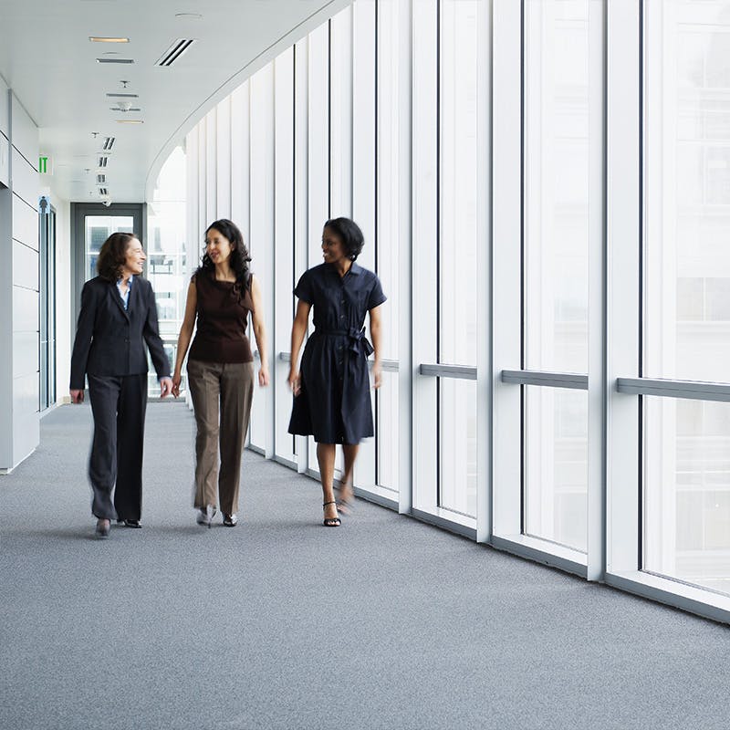 three women walking down a long hallway with windows