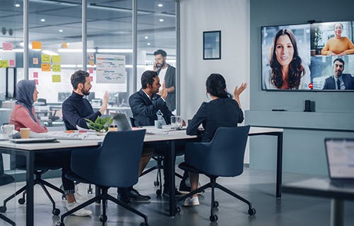 Team members in office meeting with remote workers on conference room screen