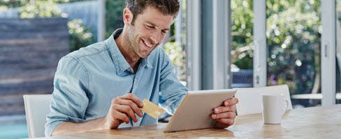 man shopping on his laptop holding credit card smiling