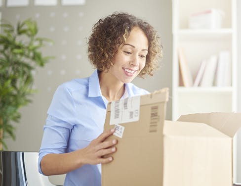 Young woman in her home office holds mail package.