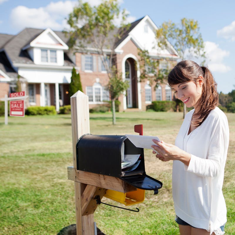 Woman grabbing mail at mailbox with sold house in background