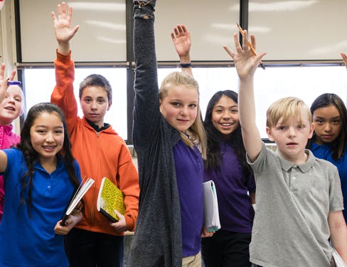 Portrait of students raising hands in classroom.