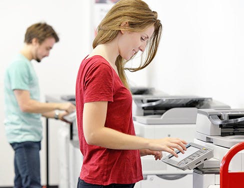 Photo of a girl in a red shirt working at a printer.