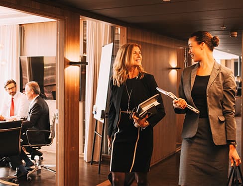 Female lawyers discussing while colleagues planning in background at law office