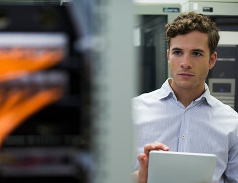 Computer technician using digital tablet performing maintenance check of mainframe equipment.