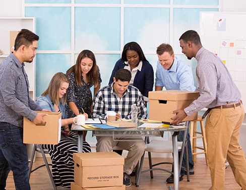 Photo of a group of people gathered around a table with boxes and documents.