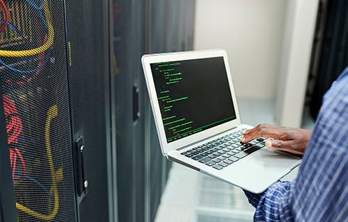 TitleCloseup shot of an unrecognizable man using a laptop while assessing system in server room