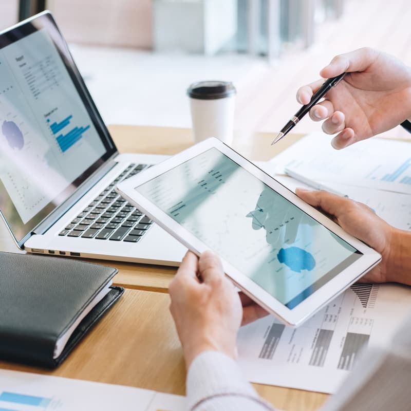Midsection Of Businessman Holding Digital Tablet Discussing With Colleague At Desk In Office