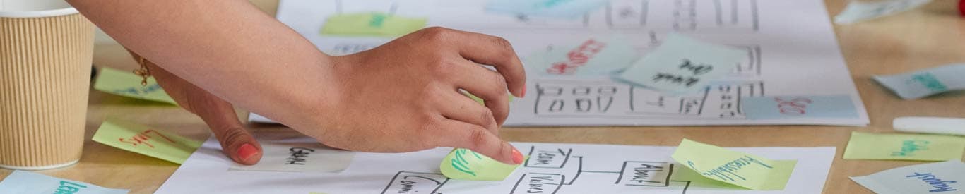 team collaboration. Close up of hands moving post it notes around a written diagram on a table