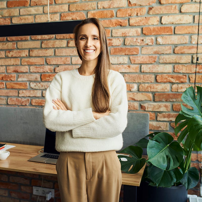 Woman standing confidently in front of her desk and brick wall
