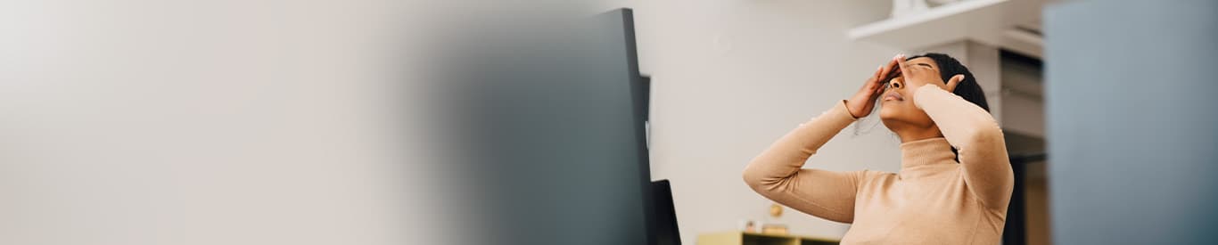 Frustrated employee in front of a computer covering her eyes