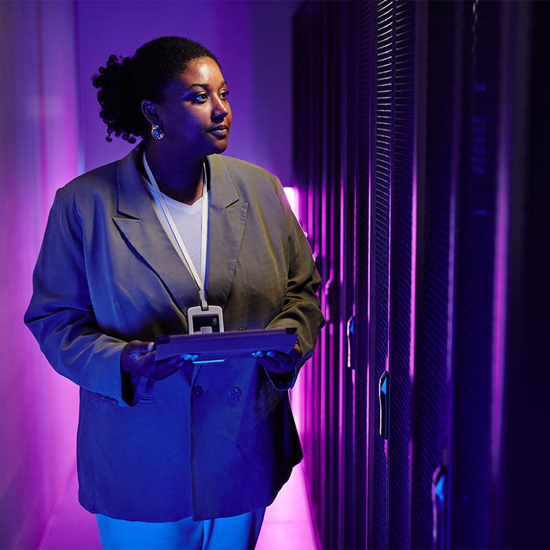 Portrait of female system administrator inspecting data network in server room lit by neon light