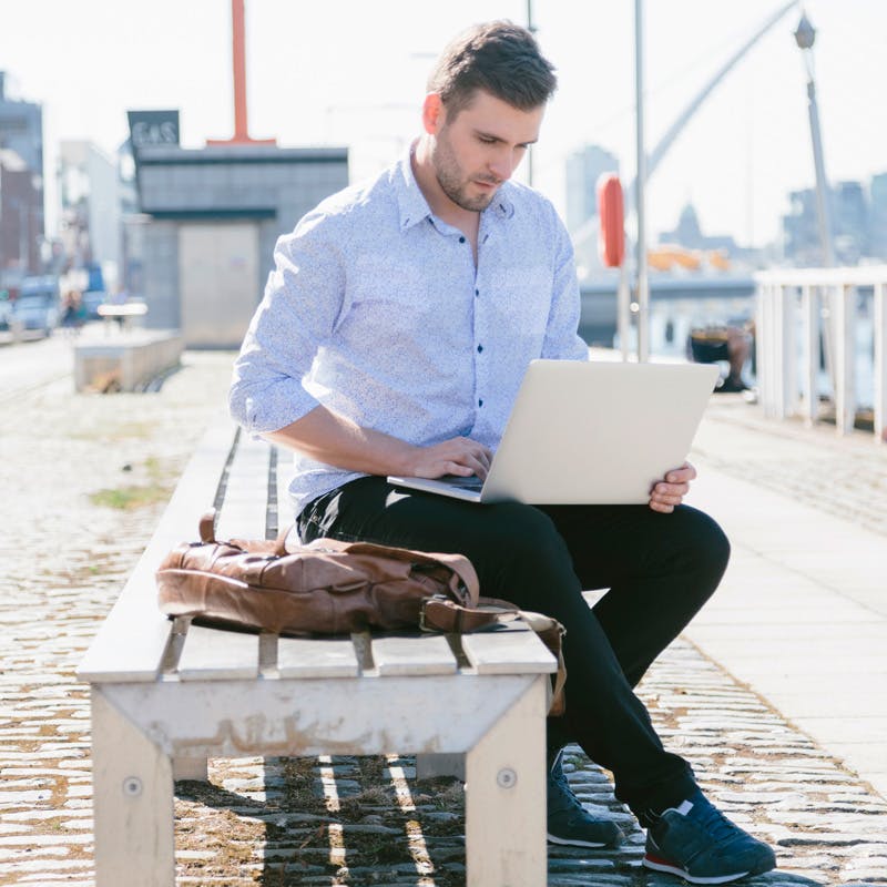 young businessman sitting on bench using laptop