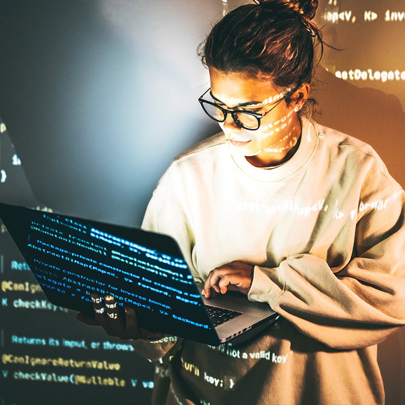 Developer standing in front of projected code while holding a laptop while giving a presentation