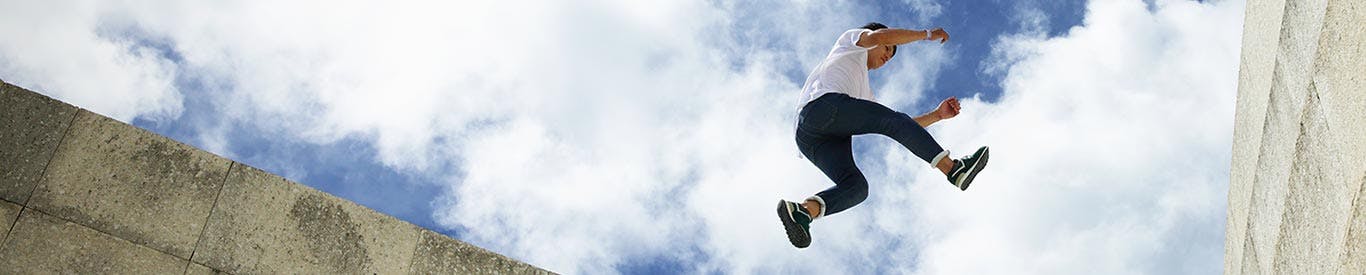 person jumping from one wall to another with a cloudy sky as the background