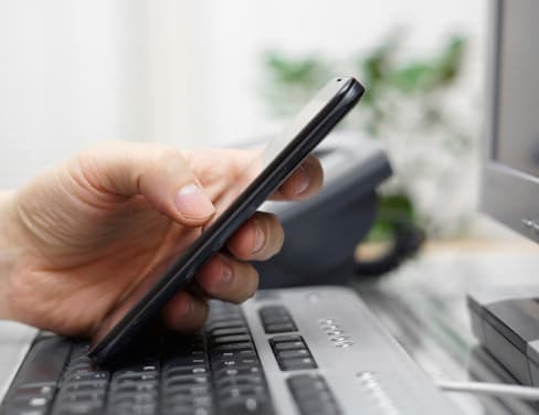 Ricoh closeup of person on mobile phone resting on keyboard