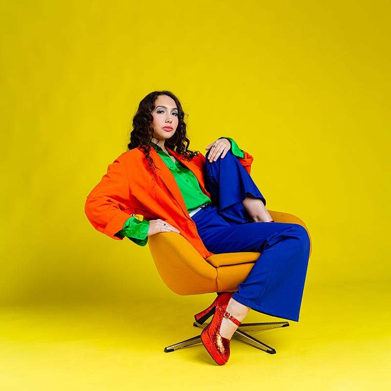 woman with a bright suit on sitting on a chair agains a yellow background