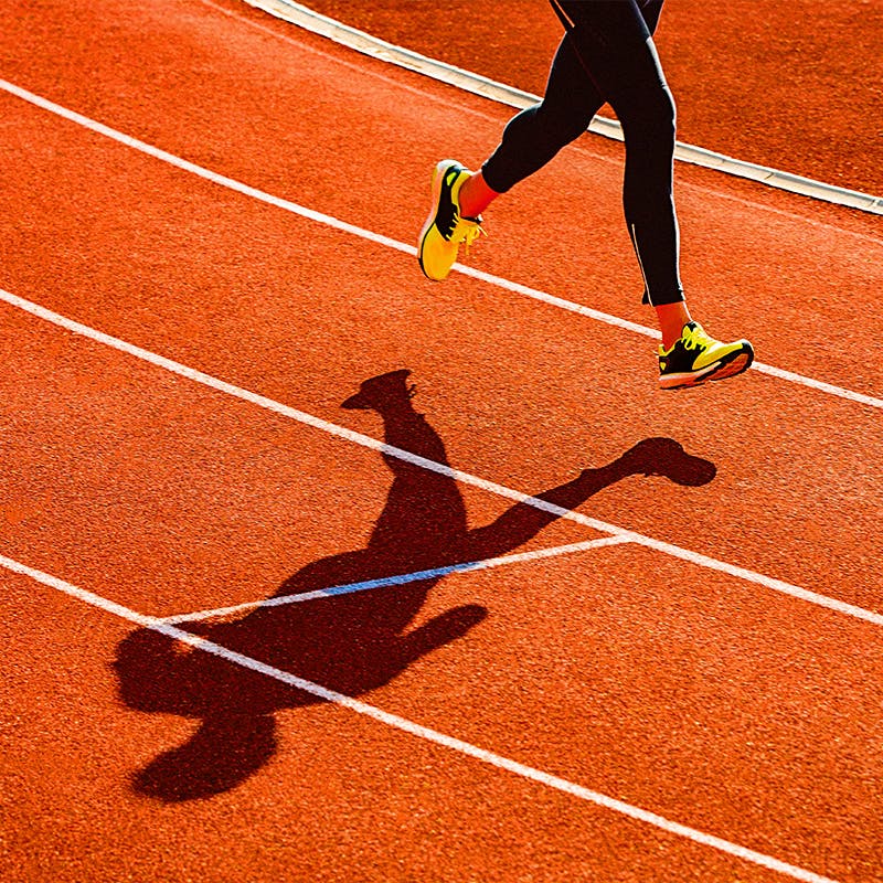 Image of a persons legs running on a track with bright colored running shoes