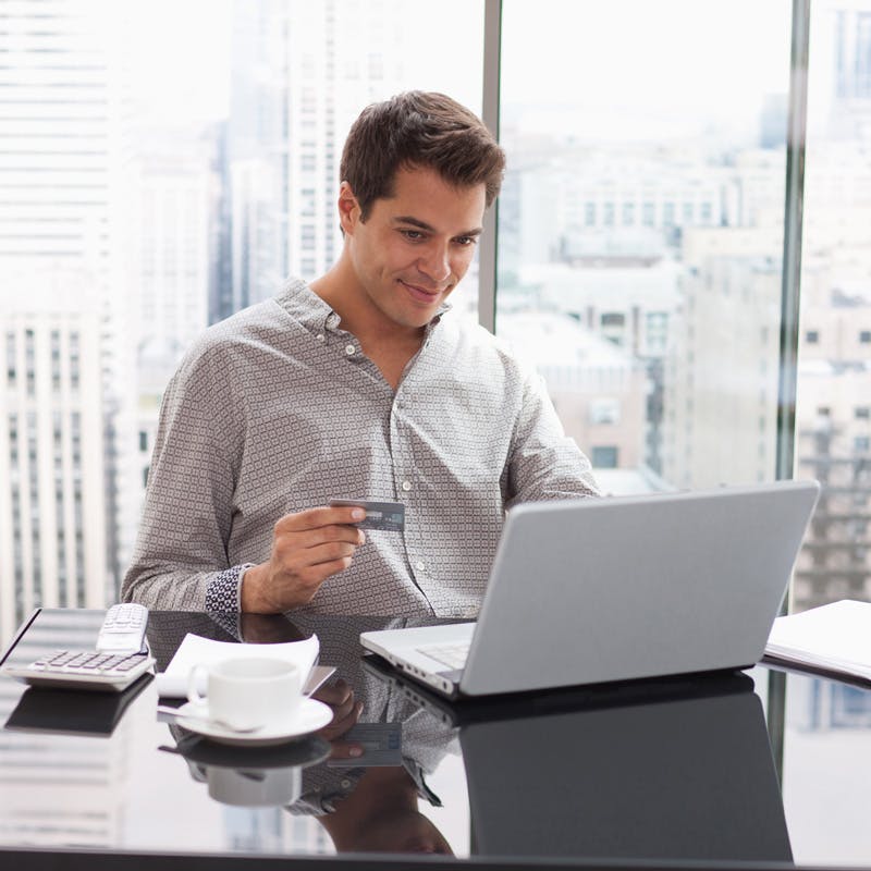 man shopping on his laptop holding credit card smiling