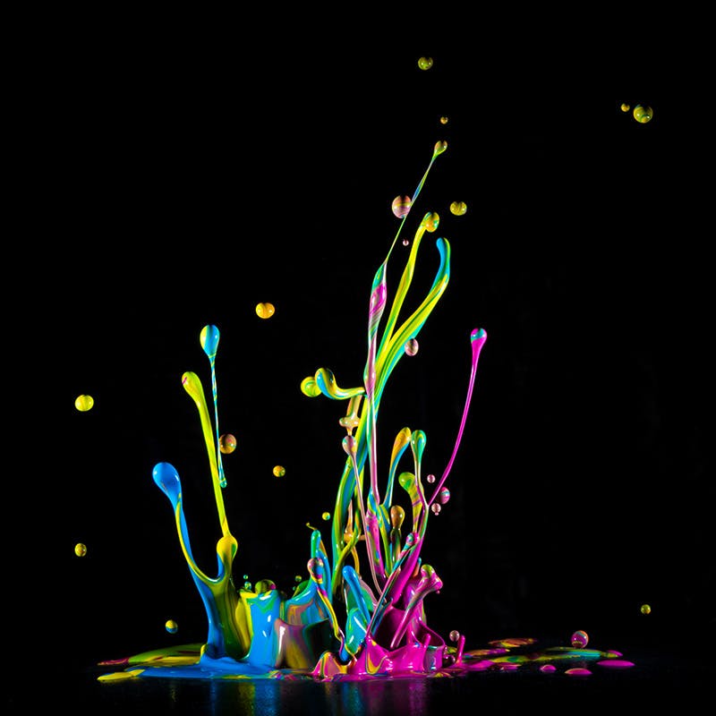 Ink splashing up in colors of cyan, magenta and yellow on a black background