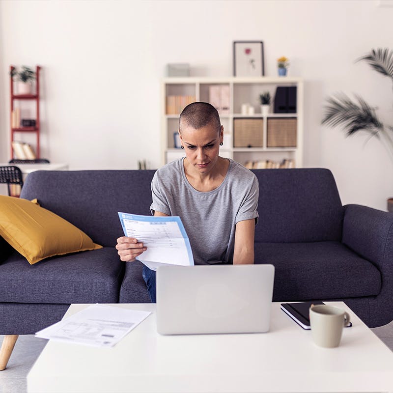 Woman paying bills online with laptop while sitting on sofa in living room
