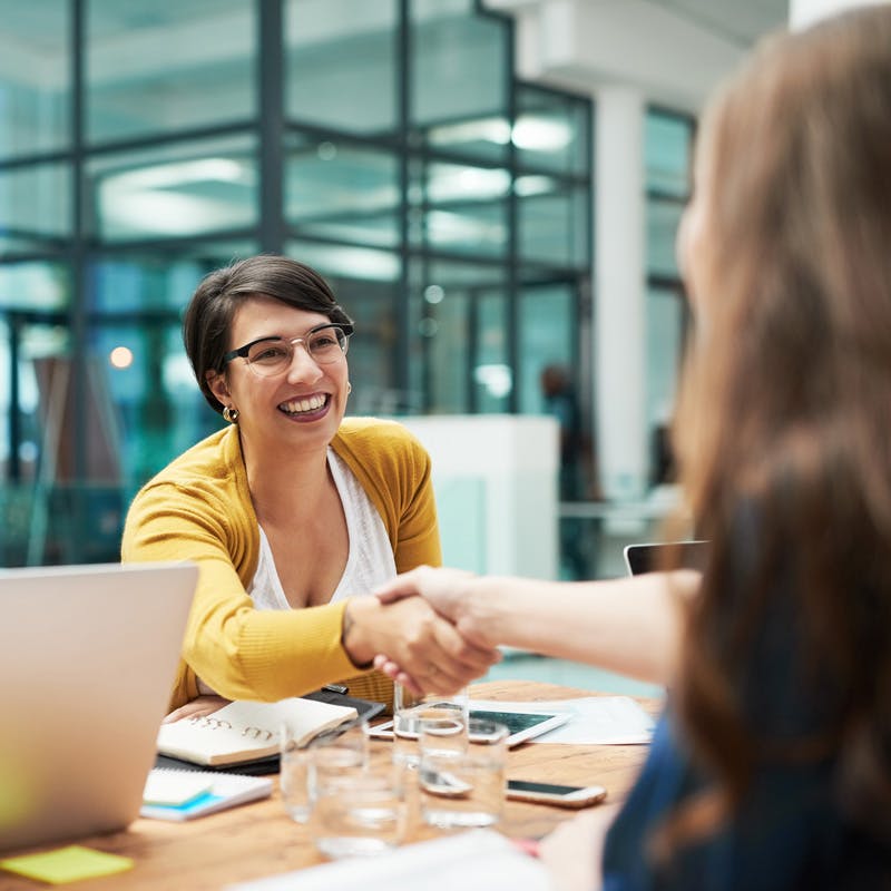 Woman giving handshake to another woman in meeting room and laptop