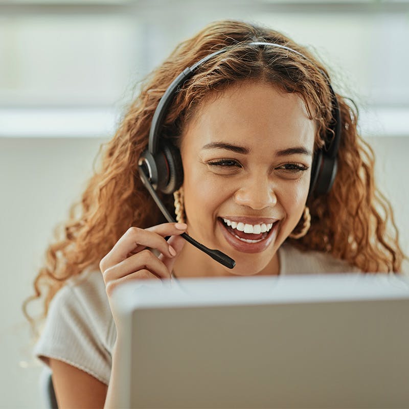 Young woman with headset on at a desktop laughing while talking to a customer