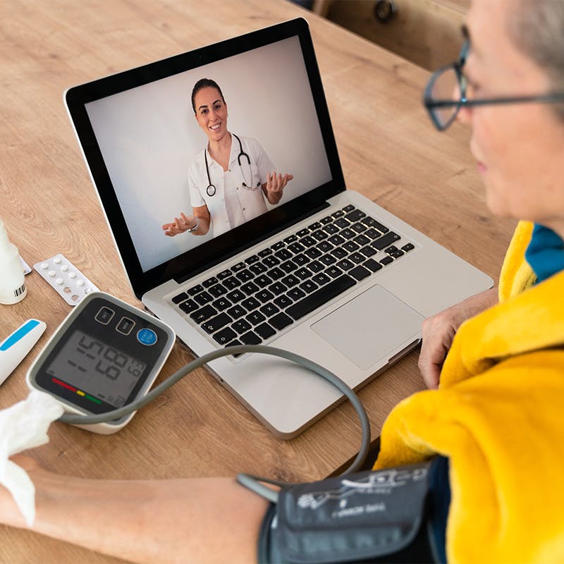 woman meeting with her doctor remotely on her laptop while checking her blood pressure
