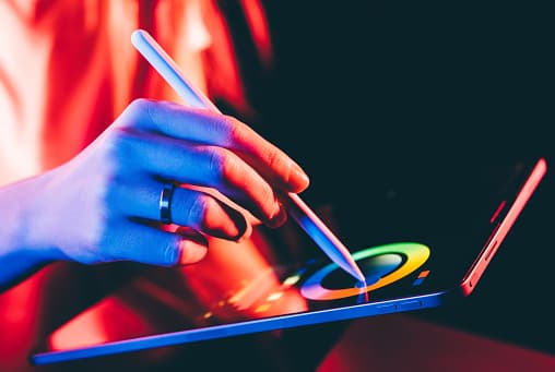 Hand using a tablet with a stylus against a black background, depicting solutions integrating print and automation.