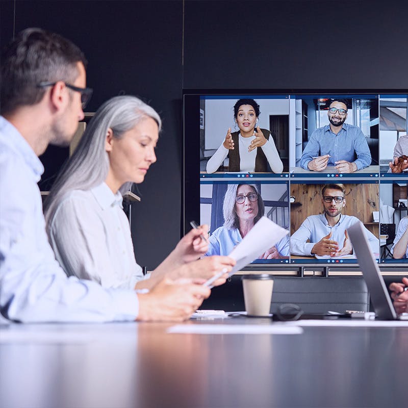 videoconference in meeting room with people sitting in modern office and  colleagues on big screen monitor. Business technologies concept.