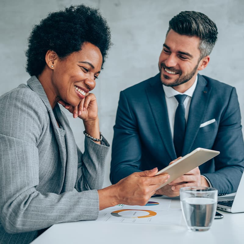 Two people at a conference table working off os a tablet