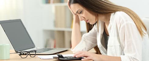 woman working at laptop with papers and calculator looking frustrated