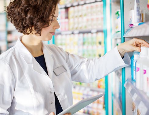 Young pharmacist with a digital tablet in drug store checking medicines on the shelf.