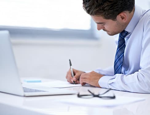 Lawyer filling up paperwork in front of laptop computer.